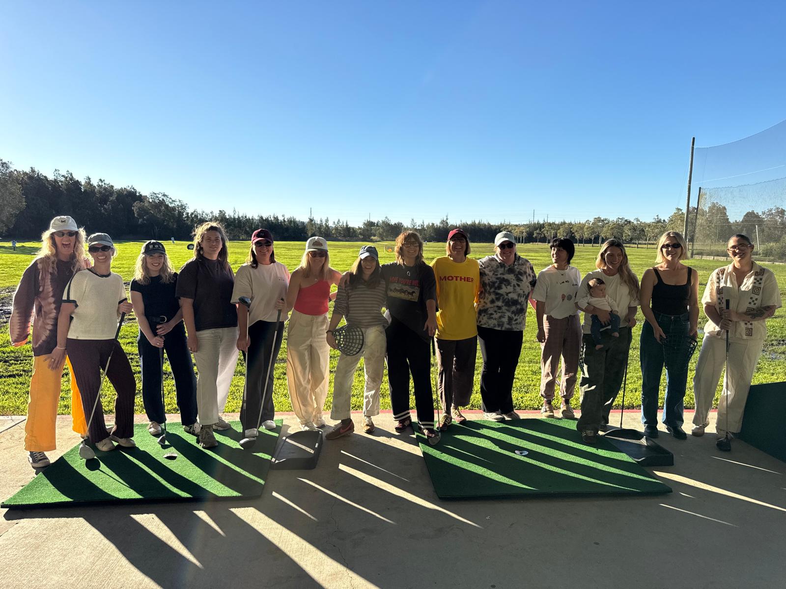 Mully group standing together at the driving range in the sunshine with clubs lined up in front