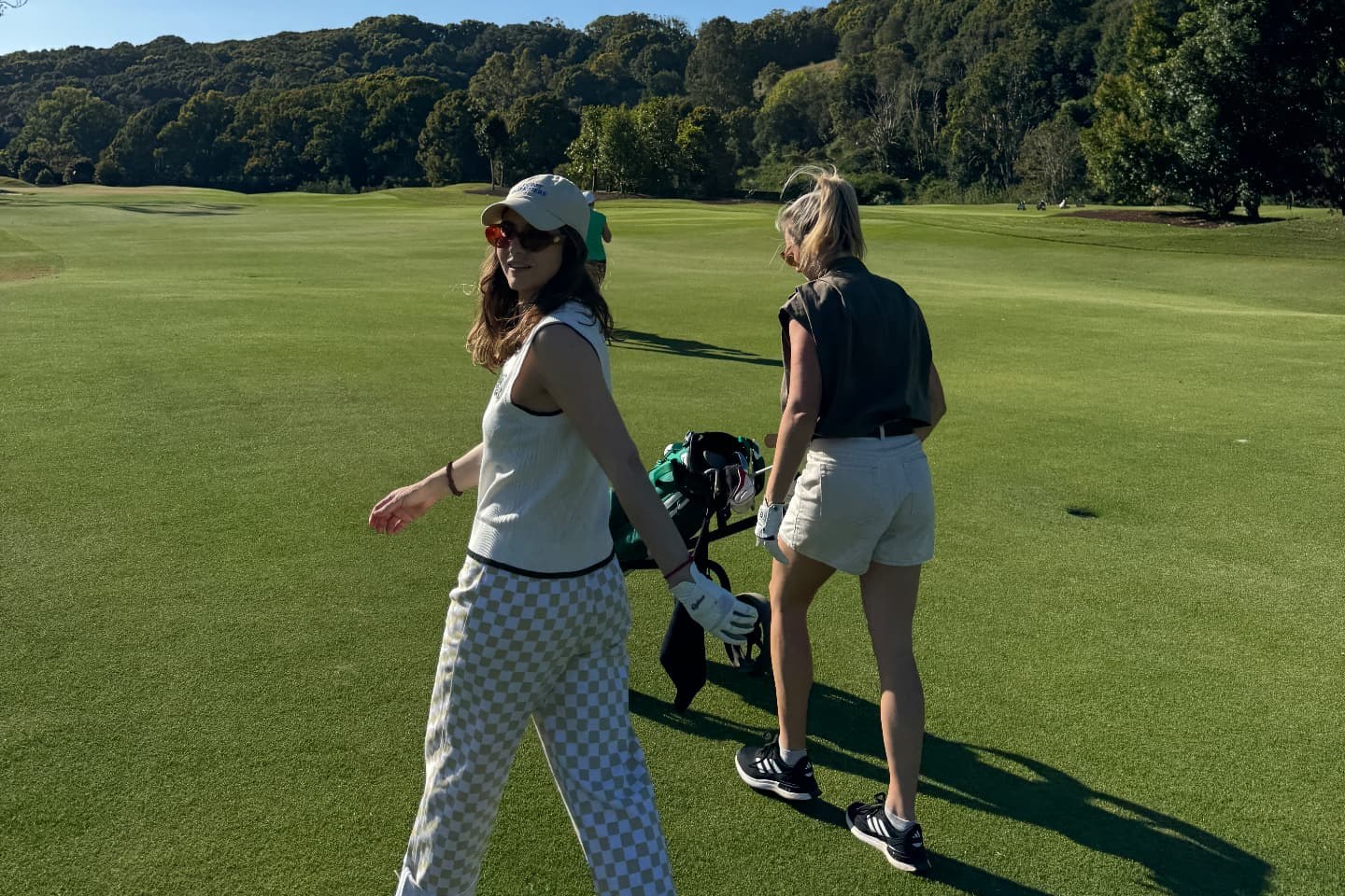 Two friends walking the fairway with a golf trolley under a blue sky