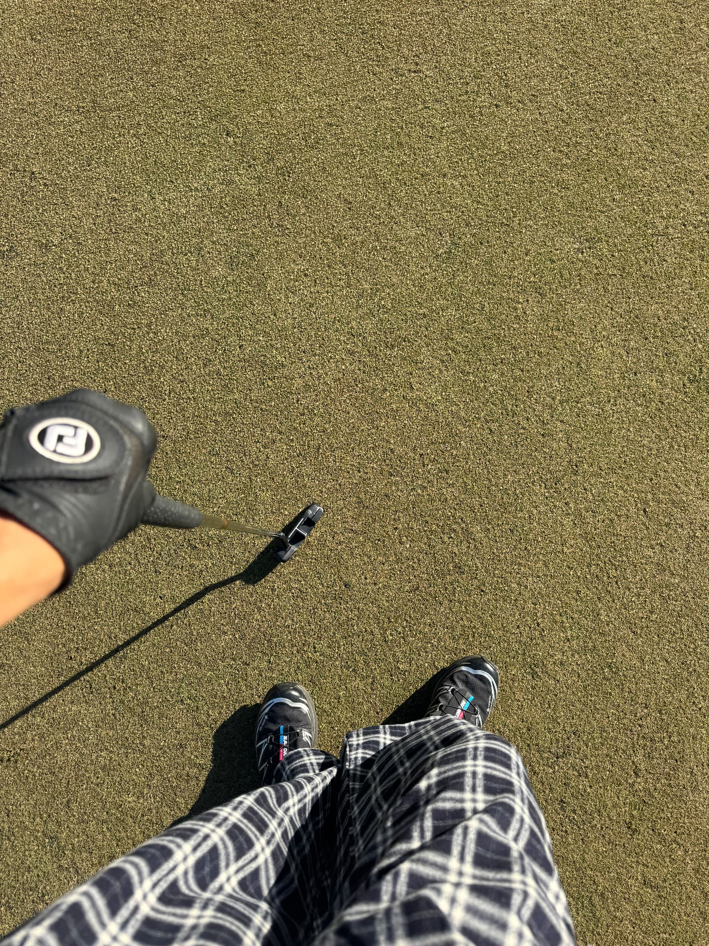 Plaid trousers, sneakers and a putter seen from above on the green