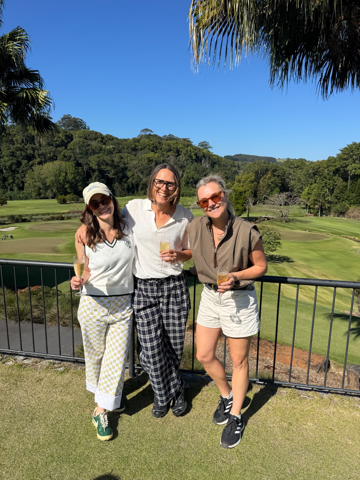 Three friends with drinks on a terrace overlooking the golf course at golden hour